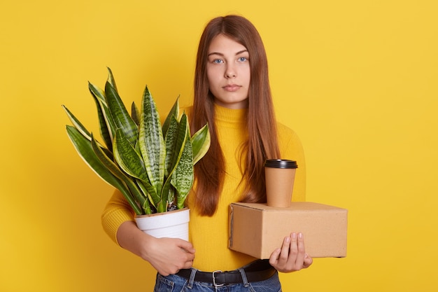 Sconvolto abiti femminili abbigliamento casual tenendo il suo personale e vaso di fiori con la canapa della corda dell'arco nelle mani sul giallo