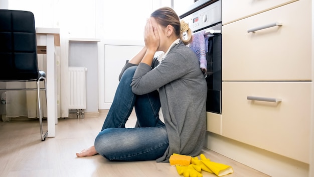 Sconvolto e stressato giovane donna seduta sul pavimento in cucina e piangendo.