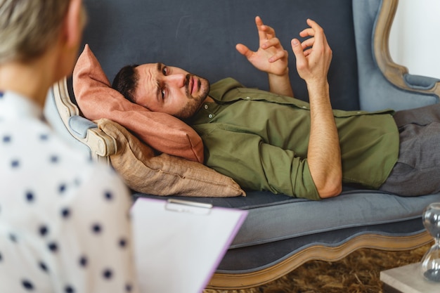 Sconvolto giovane paziente maschio caucasico dai capelli scuri che si lamenta dei suoi problemi psicologici con una psicoterapeuta femmina