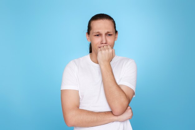 Sconvolto giovane ragazzo in t-shirt ha dimenticato qualcosa o ha commesso un errore isolato su sfondo blu. Rimpiange di aver sbagliato