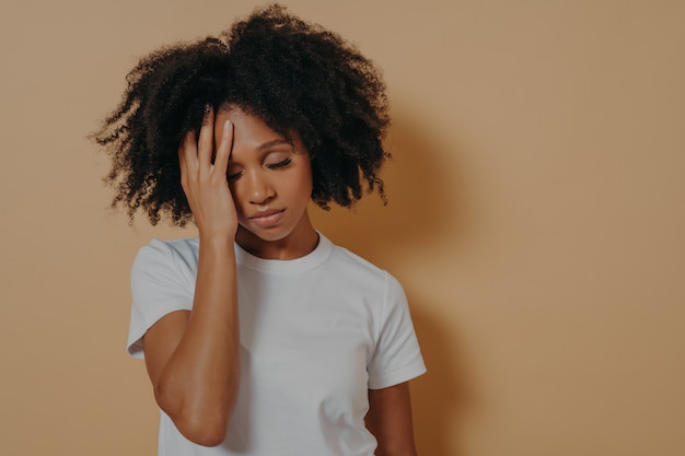 Sconvolto stanco cark scuoiato femmina avendo mal di testa dopo il superlavoro, isolato su beige studio wall