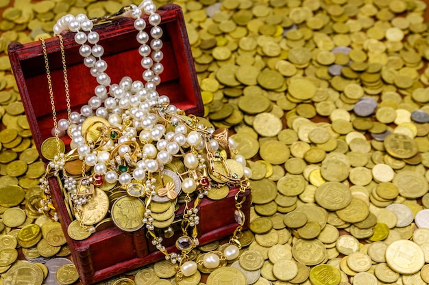 Scrigno d'epoca pieno di monete d'oro e gioielli su uno sfondo di monete d'oro