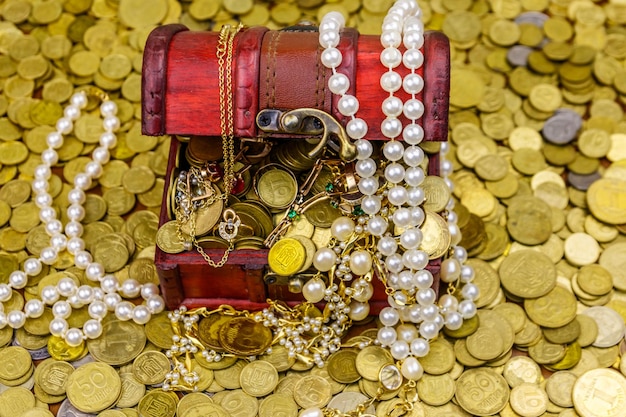 Scrigno d'epoca pieno di monete d'oro e gioielli su uno sfondo di monete d'oro