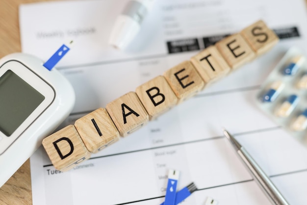 Scritta DIABETE su cubi di legno con glucometro in pillole e test della glicemia sul tavolo