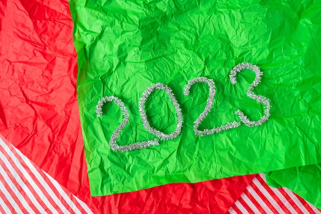 Scritte 2023 dalla scintillante pioggia di ghirlande su sfondo rosso e verde di carta da regalo Decorazioni di Capodanno e Natale