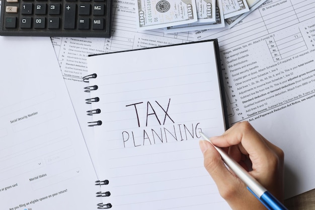 Scrittura a mano della pianificazione fiscale come promemoria sul tavolo di lavoro con moduli fiscali denaro e calcolatrice