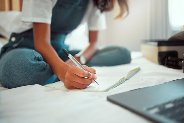 Scrittura a mano e taccuino con una donna su un letto a casa sua mentre scrive sul blog studiando o facendo ricerche Camera da letto relax e laptop con una studentessa che tiene in mano una penna durante una ricerca o una pianificazione