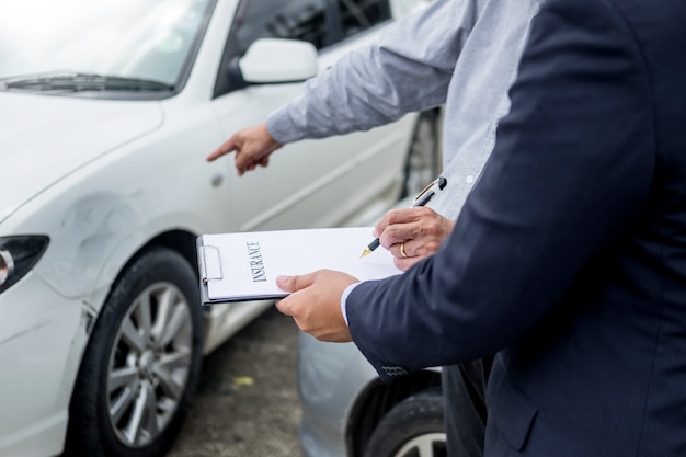 Scrittura dell&#39;agente di assicurazione sui appunti mentre esaminando automobile dopo l&#39;incidente