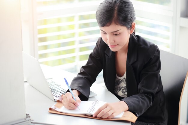 Scrittura della donna di affari sul taccuino con il computer portatile