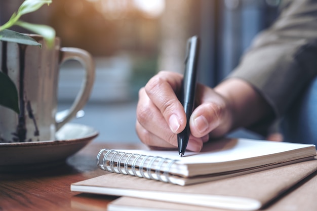 scrittura della mano della donna sul taccuino in bianco con la tazza di caffè sulla tavola di legno