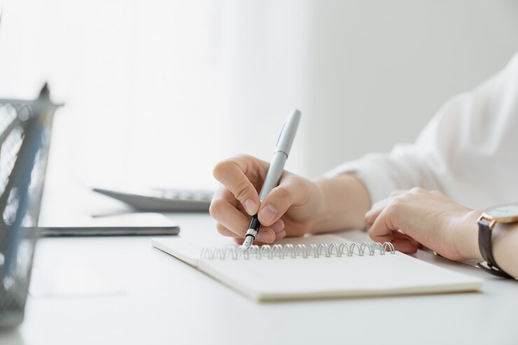 Scrittura della mano della donna sul taccuino in bianco sulla tavola in casa.