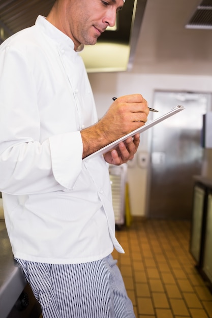 Scrittura maschio concentrata del cuoco sulla lavagna per appunti in cucina