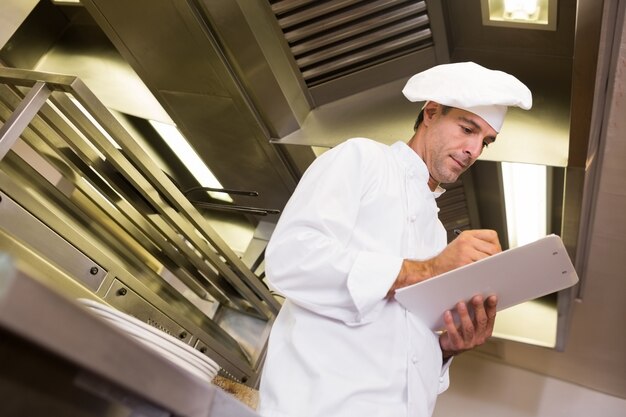 Scrittura maschio concentrata del cuoco sulla lavagna per appunti in cucina