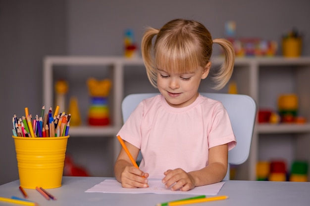Scrittura sveglia della ragazza del bambino con le matite nel centro di assistenza diurna