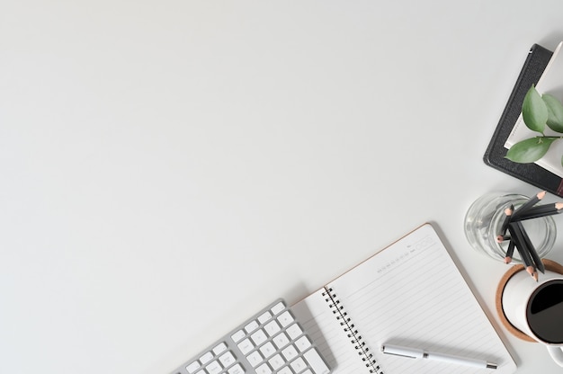 Scrivania con il computer della tastiera dello spazio della copia di vista superiore, il caffè, la carta del taccuino e gli articoli per ufficio sulla scrivania.