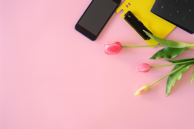 Scrivania con taccuino a fiori di tulipano per laptop e penna sul pavimento rosa vista dall'alto piatto