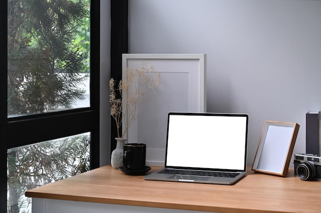 Scrivania da casa con computer portatile, cornice vuota e pianta in vaso.