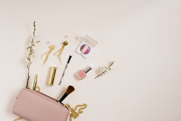 Scrivania da donna con cosmetici che si trova accanto a una borsa rosa o a una borsa per cosmetici con spazio per copiare fiori di melo su uno sfondo beige