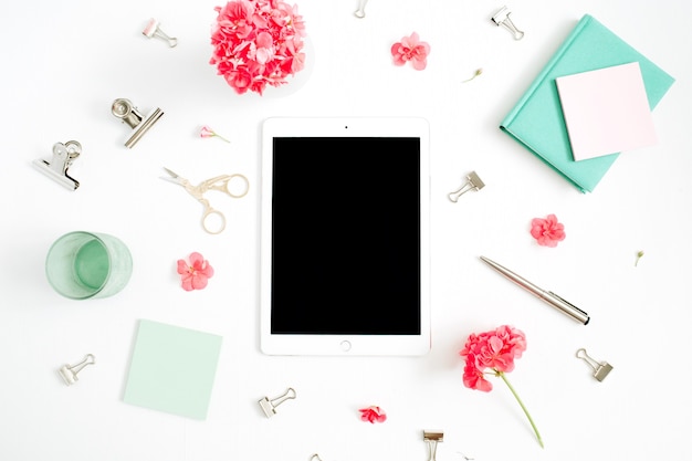 Scrivania da ufficio moda piatta. Area di lavoro femminile con tablet schermo vuoto, fiori rossi, accessori, diario di menta su bianco