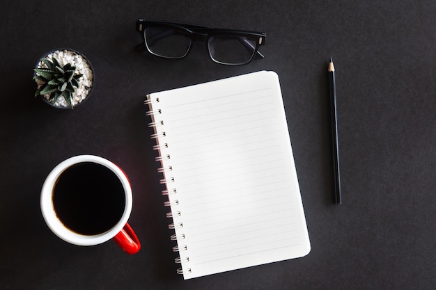 Scrivania da ufficio nera con tazza di caffè, cactus, occhiali, matita e taccuino