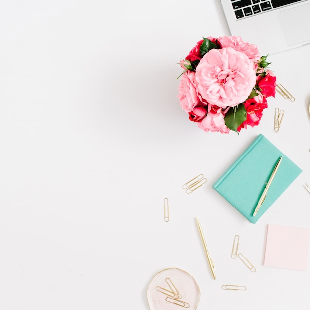 Scrivania da ufficio piatta. Area di lavoro femminile con laptop, bouquet di rose rosa e rosse, accessori dorati, diario di menta su bianco