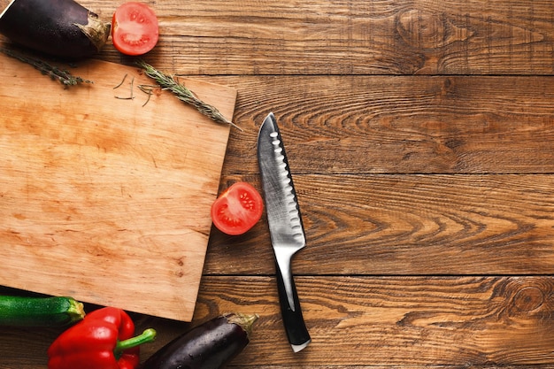 Scrivania in legno con coltello, verdure e spezie su fondo rustico, vista dall'alto, copia spazio.