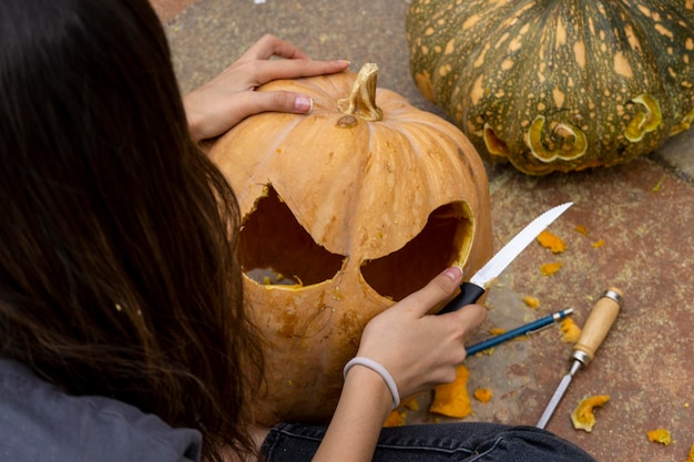 Scultura femminile grande zucca arancione per Halloween mentre si siede al tavolo di legno a casa