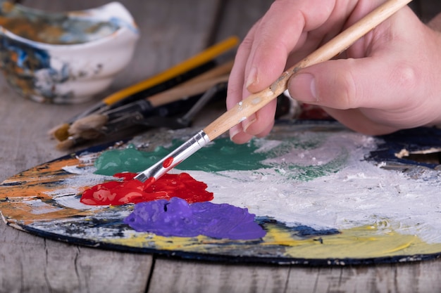 Scuola d'arte. Primo piano della tavolozza di legno con vernice acrilica e pennello in mani dell'artista.