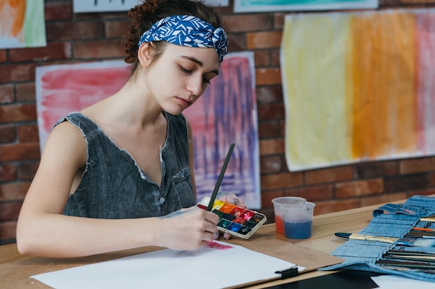 Scuola d'arte Ritratto di giovane donna che dipinge con acquerello in studio Sfoca le opere d'arte colorate sullo sfondo