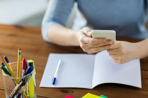 scuola superiore, istruzione, persone e concetto di apprendimento - primo piano di giovane studente o donna con smartphone e libro che scrive sul taccuino a casa