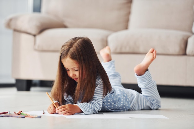 Sdraiato sul pavimento e disegnando Bambina carina al chiuso a casa da sola