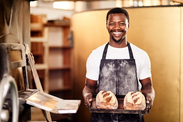 Se vuoi qualcosa di fresco, vieni nella mia panetteria Foto ritagliata di un panettiere maschio che tiene in mano il pane appena sfornato nella sua panetteria
