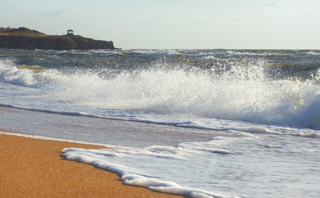 Sea surf grande onda sulla costa e promontorio con padiglione a distanza