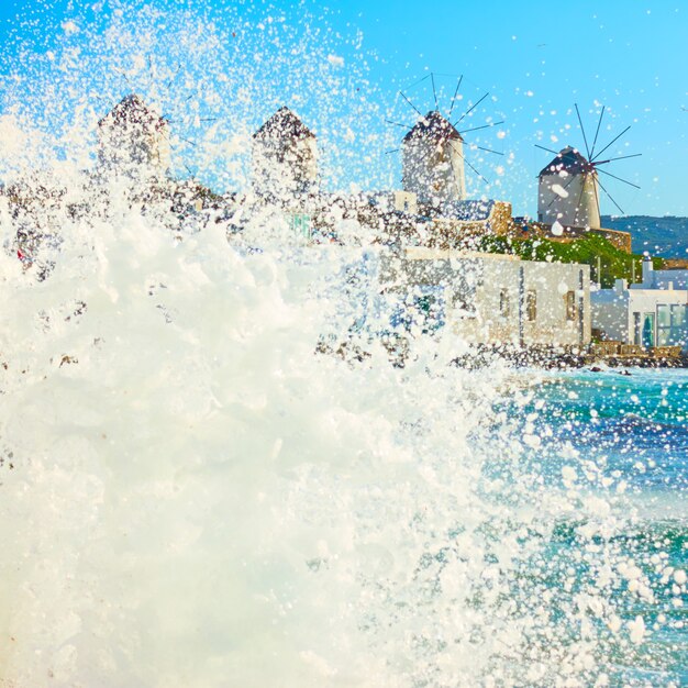 Sea surf splash e windmillls sulla costa del Mar Egeo a Mykonos, Cicladi, Greece