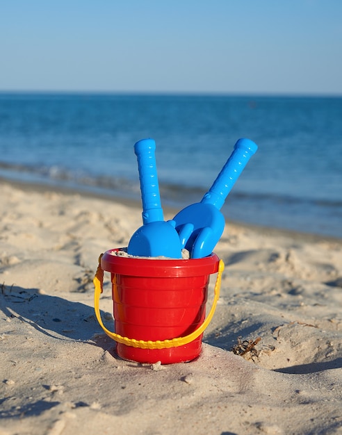 Secchio di plastica rosso bambino con sabbia e pala in riva al mare