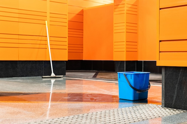 Secchio e mop di plastica blu sulla stazione della metropolitana vuota con le pareti arancio.