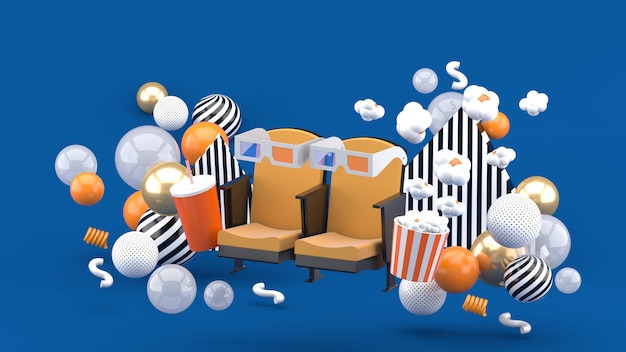 Sedia da cinema Bevande analcoliche e popcorn tra le palline colorate sul blu. Rendering 3d.