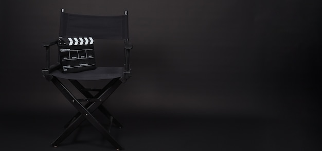 Sedia da regista nera e ciak o ardesia cinematografica. Uso IT nella produzione video o nell'industria cinematografica e cinematografica. È di colore nero.