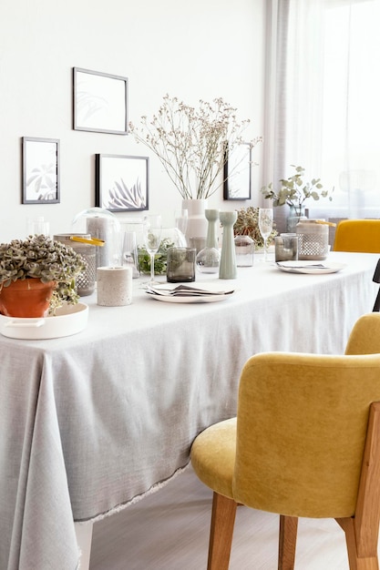 Sedia gialla a tavola con stoviglie nell'interiore luminoso della sala da pranzo con fiori e poster Foto reale