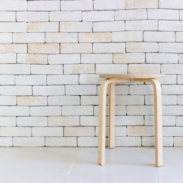 Sedia in legno nella stanza bianca vuota contro un muro di mattoni