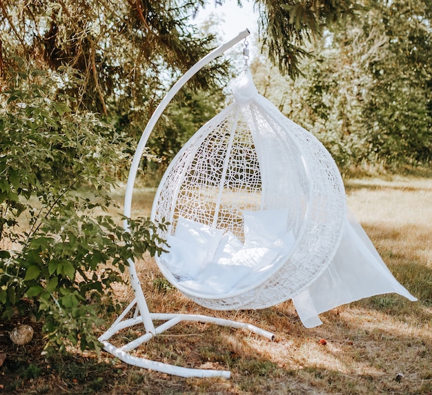 Sedia pensile a baldacchino Photozone nella foresta in natura. il tessuto svolazza al vento. Posto per una foto della sposa. sessione fotografica