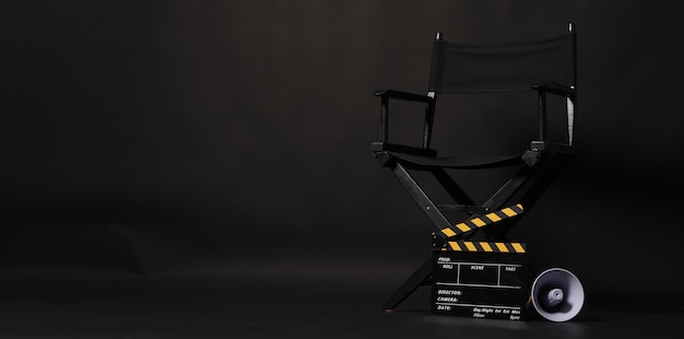 Sedia regista nera e batacchio o ciak film con megafono giallo su sfondo nero. utilizzare nella produzione video o nell'industria cinematografica