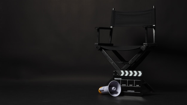 Sedia regista nera e ciak o ciak film con megafono su sfondo nero. utilizzare nella produzione video o nell'industria cinematografica