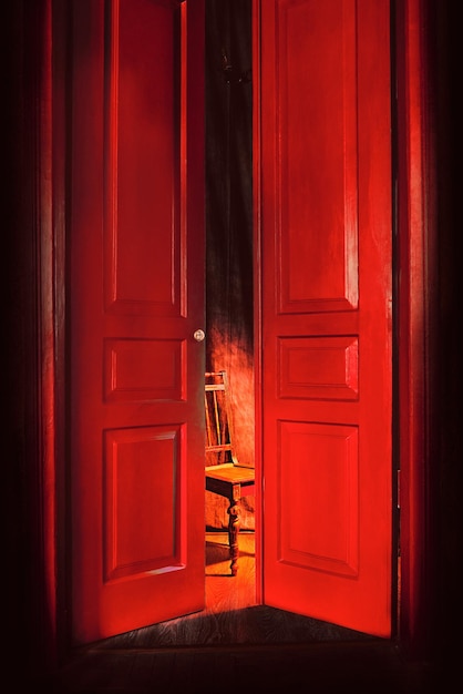 sedia vuota in luce dietro enormi porte vintage rosse per interni Concetto di interni vecchio stile