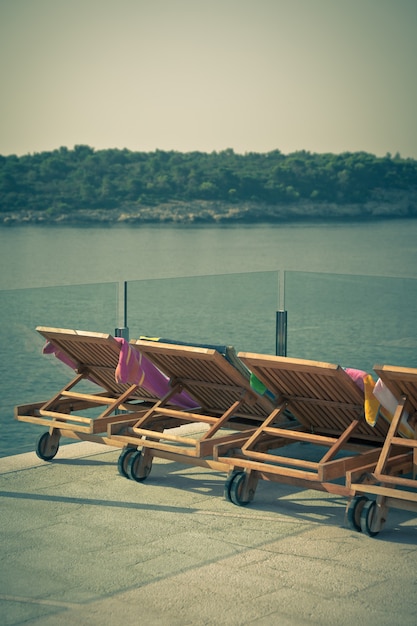 Sedie a bordo piscina dell'hotel con vista sul mare. Scatto verticale in stile vintage