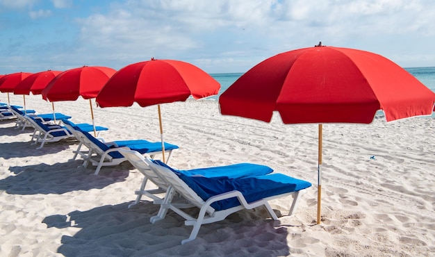 Sedie a sdraio blu e ombrelloni rossi sulla spiaggia del mare in estate