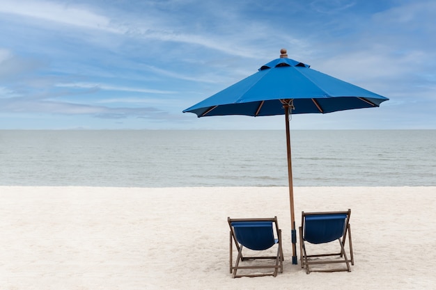 Sedie a sdraio e ombrellone blu con cielo blu sulla spiaggia dell'isola tropicale