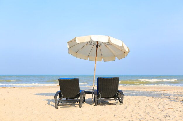 Sedie a sdraio sulla spiaggia di sabbia con ombrellone bianco su sole e cielo blu nuvoloso