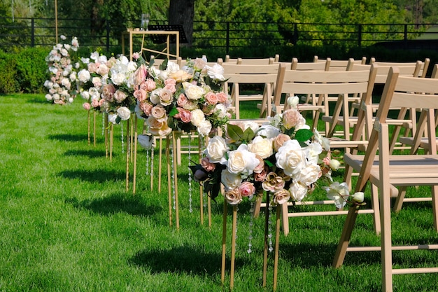 Sedie vuote di legno bianche in una fila e mazzi dei fiori su erba verde. Decorazioni per cerimonie nuziali.