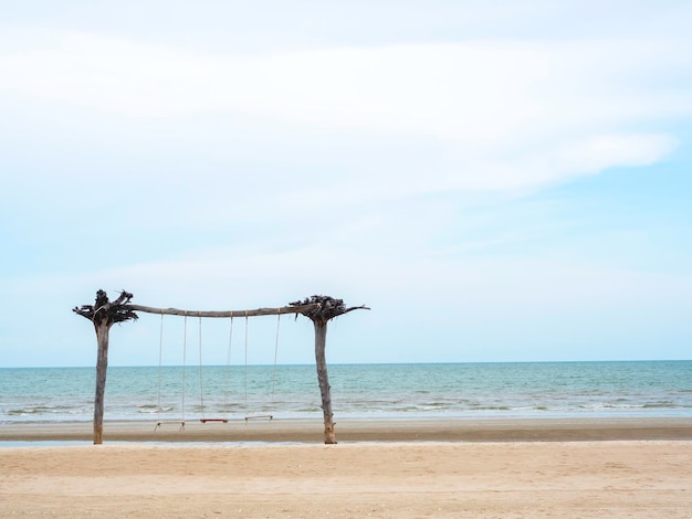 Sedile a dondolo gemello in legno vuoto sulla spiaggia su sfondo marino, sabbia, mare e cielo blu, con spazio per la copia in stile minimale